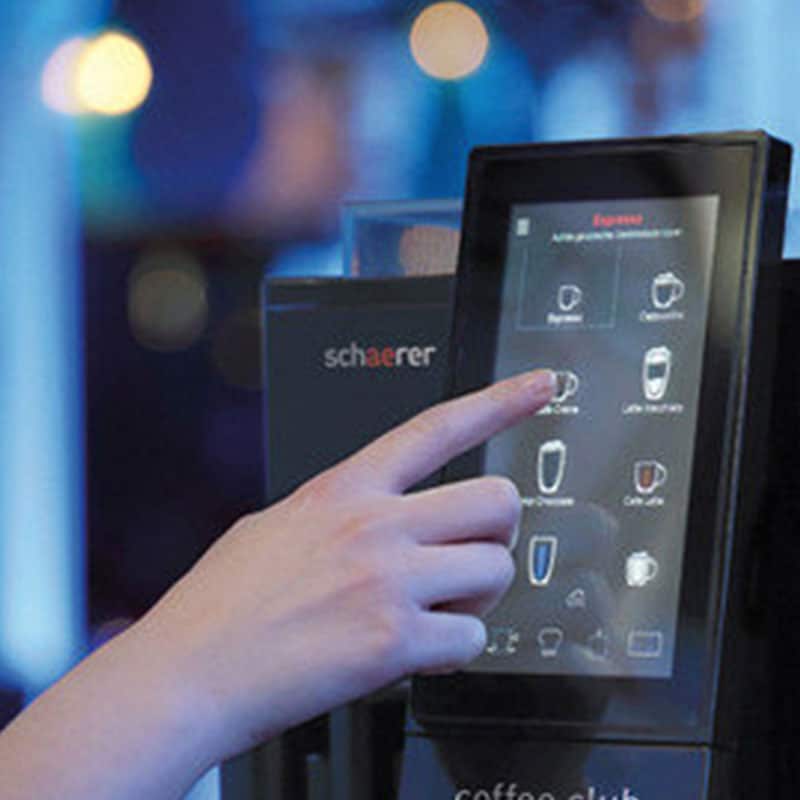 A hand selects a coffee option on a touchscreen menu of a modern coffee machine.