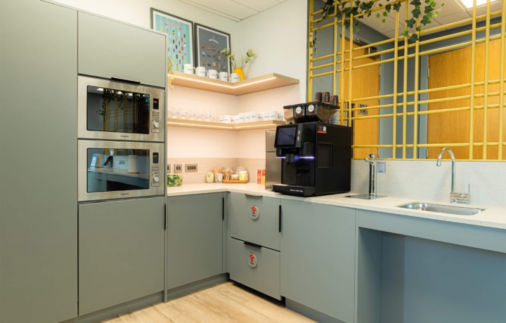 Corner view of Modern kitchen with light blue cabinets, built-in ovens, a coffee machine, and a sink